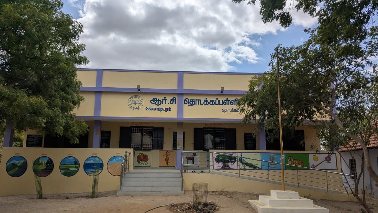 Front elevation of the completed school block showing the signage band, window openings and the full run of painted mural panels along the compound wall.